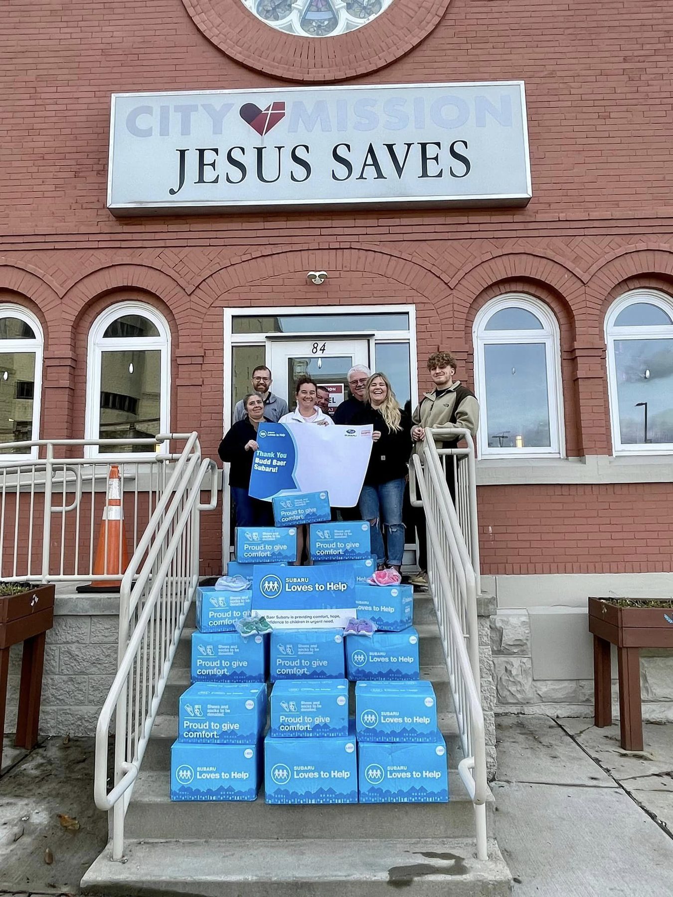 Staff outside City Mission of Washington with a thank-you sign and boxes of donated shoes